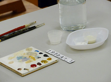 Conservation grade paint on a tile, alongside paintbrushes and a bottle of ethyl methacrylate copolymer